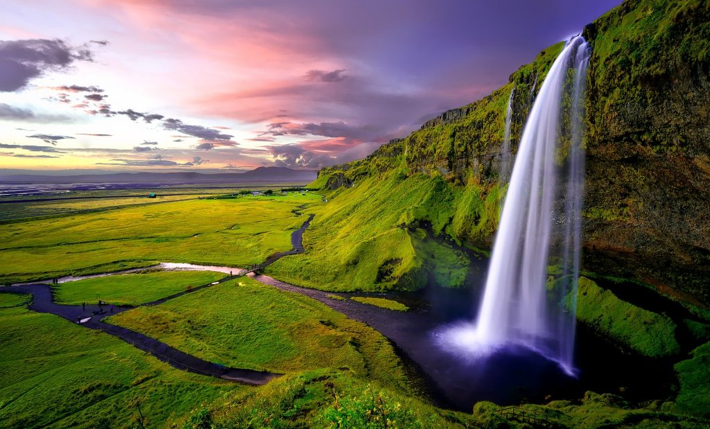 large seljalandsfoss waterfall surrounded by green fields and small river seen during sunset in iceland