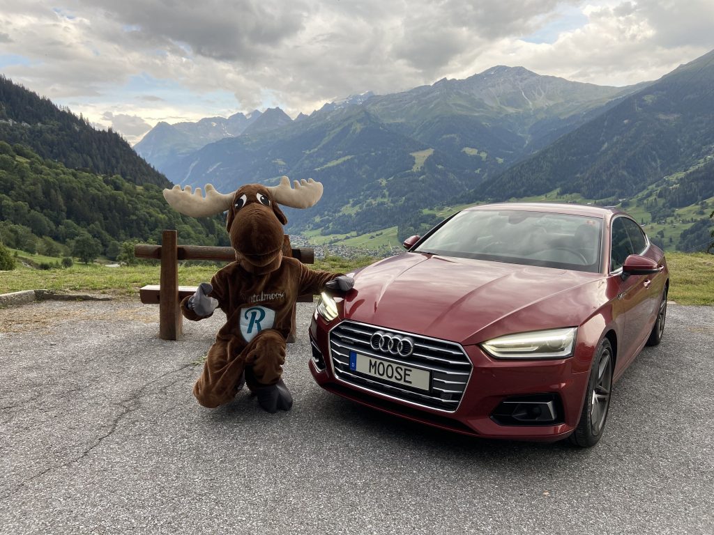 Rentalmoose posing with red Audi rental car, Swiss Alps in the background. Rentalmoose is a global rental car broker.