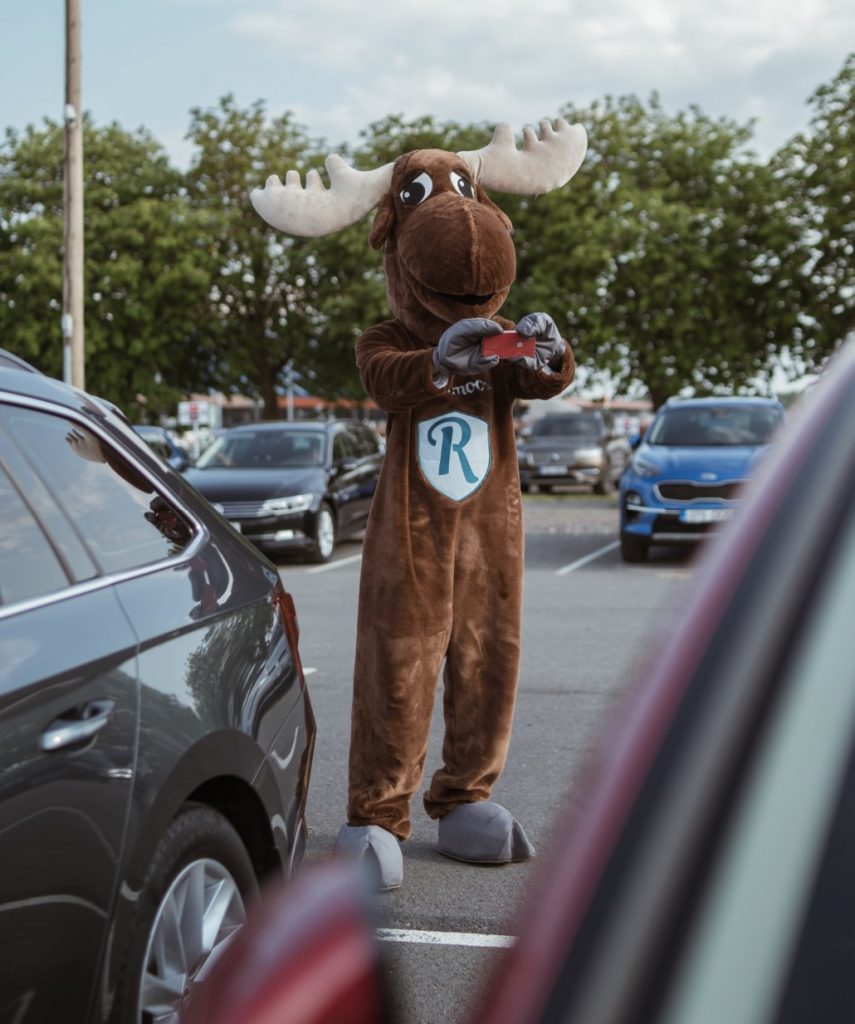 Rental Moose mascot holding red Iphone and photographing condition of rental car. Its important to always take check-in photos of the rental car when you pick it up.