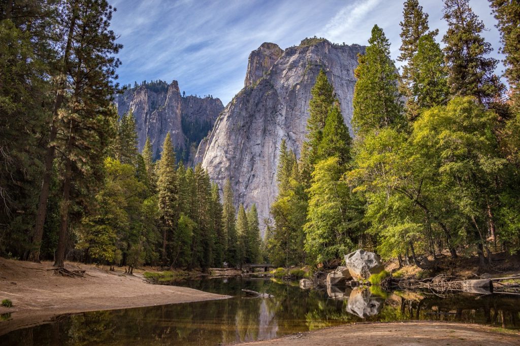 green pinetrees and small river with grand boulders in the background. The scenic beauty of Yosemite Valley in California attracts thousands of tourists every day.