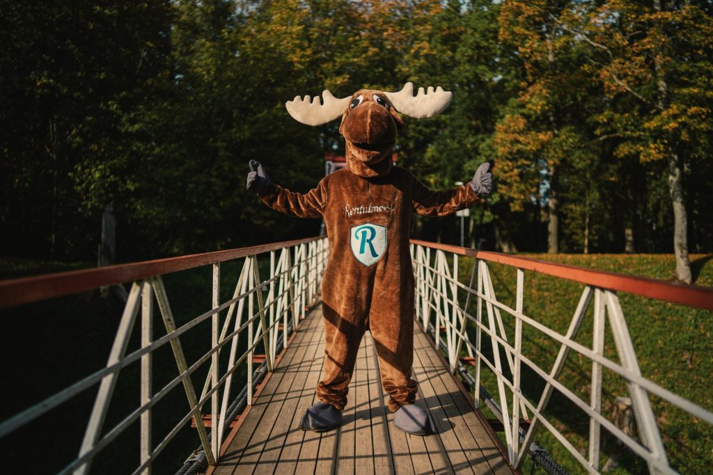 Rental Moose mascot posing with open arms on wooden bridge in a forest in estonia.