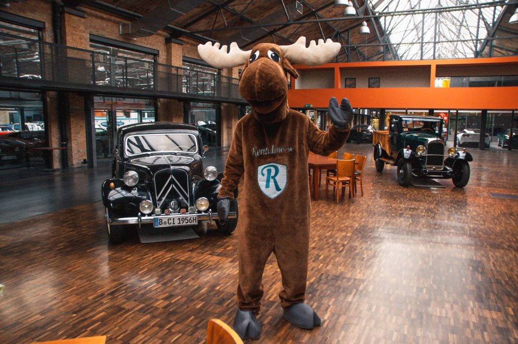 Rental Moose mascot posing in Classic Remise next to vintage cars. Classic Remise Berlin is a great spot to visit in Berlin for car enthusiasts, hundreds of classic cars can be found here.