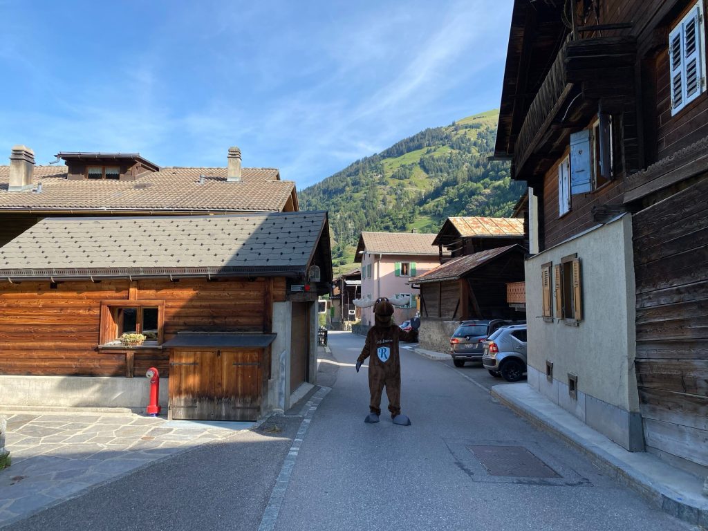 Rental Moose Mascot posing with traditional Swiss wooden homes in Verbier Village in Switzerland