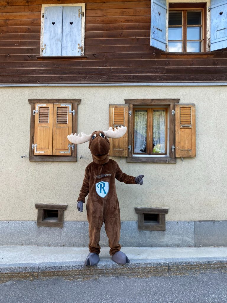 Rental Moose mascot standing next to traditional italian home in italy. See the best places to see in Italy with rentalmoose