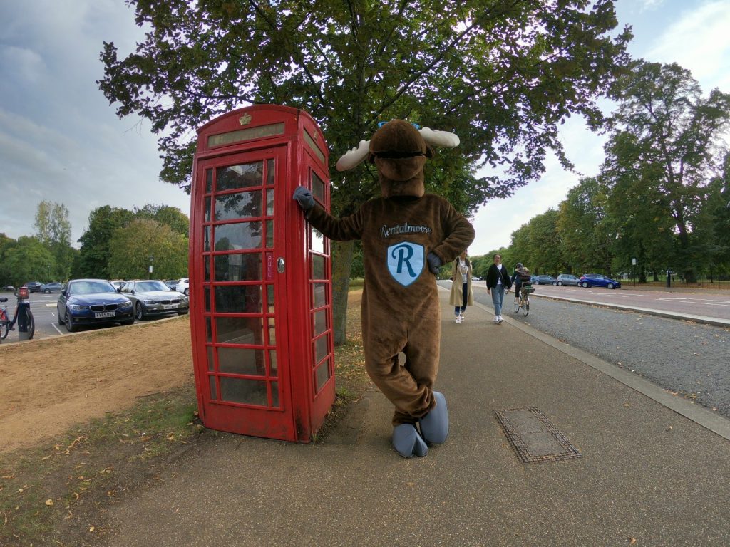 Rental Moose mascot posing with red telephone booth in London, UK. See London during our UK road trip itinerary.