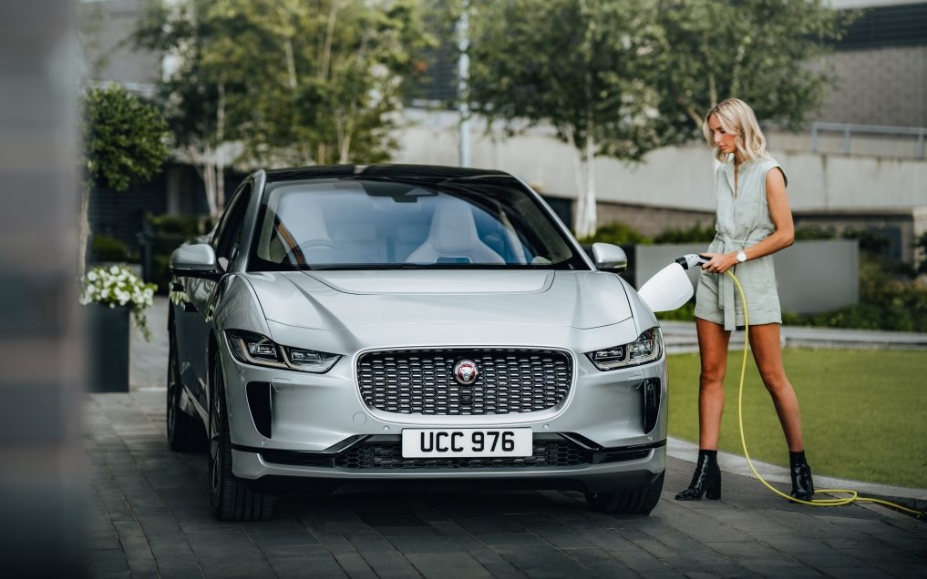 Blonde woman charging Jaguar electric car with a level 2 charging point- which is one of the quickest ways to charge an electric car.